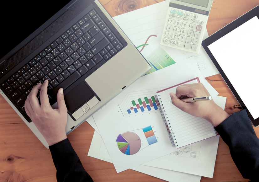 Businesswoman hand typing on laptop keyboard and analyzing business report, working over wooden desk in office in vintage color filter